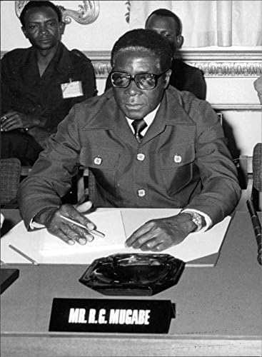 Гроздобер фотографија на Роберт Мугабе како седи на стол со неговата плоча пред себе.